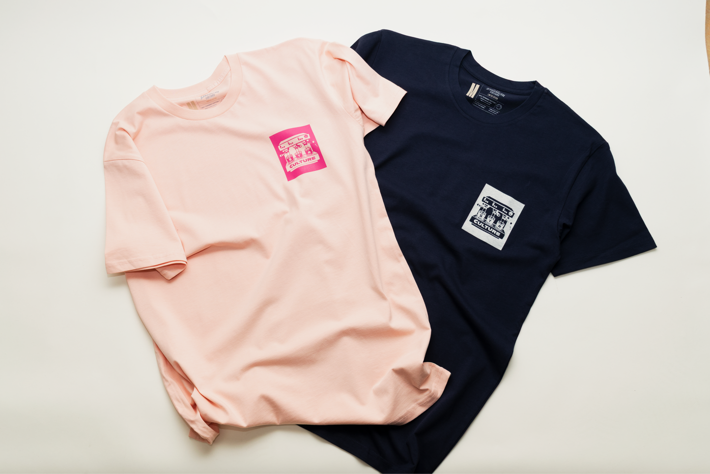 Two t-shirts, one pink and one navy, with small logos on a light background